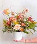 Valentine’s Day bouquet “The Flirty Little Number” by Arianna Floral Design in Boulder, Colorado, featuring peach roses, pink seasonal flowers, and greenery in a white vase.